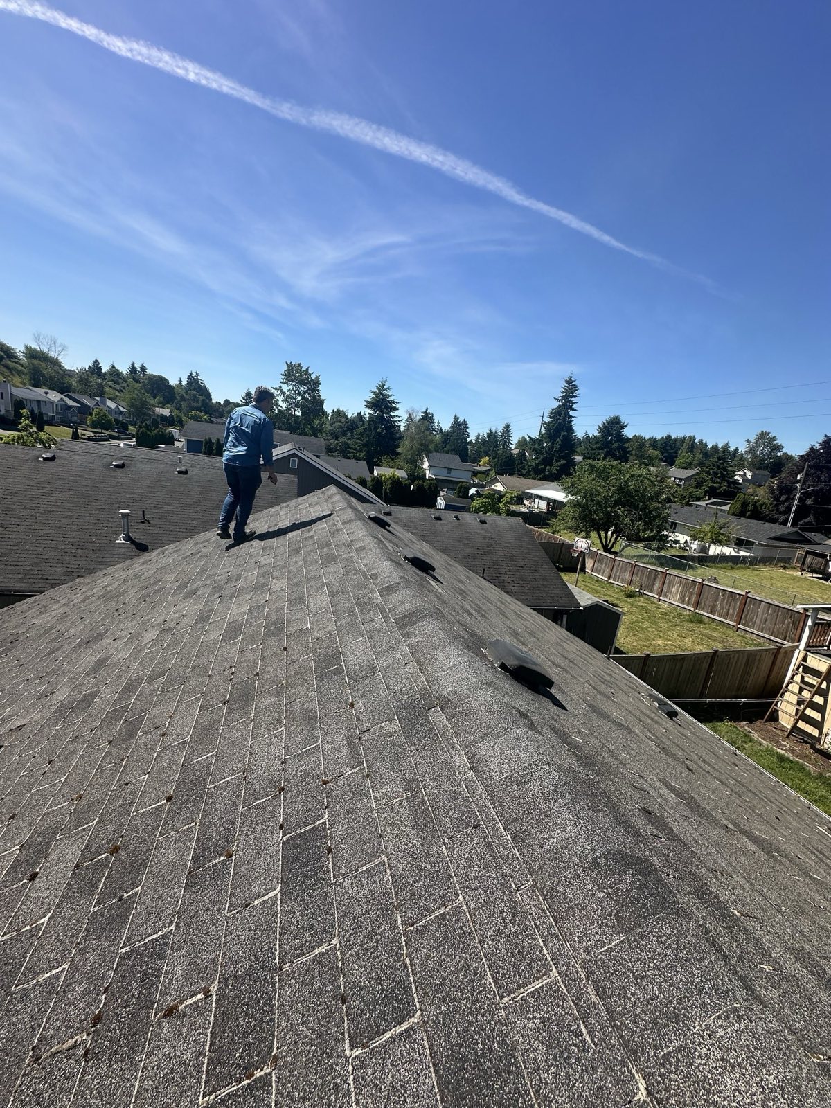 Bullock Builders crew member at work on a new asphalt shingle roof under a blue sky